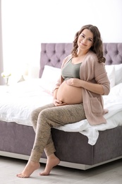 Young pregnant woman sitting on bed at home