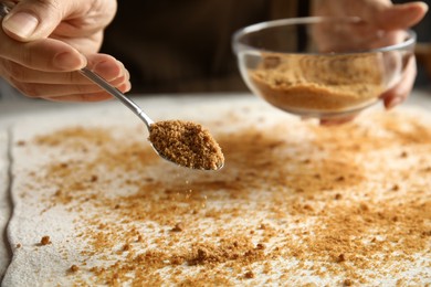 Woman pouring brown sugar onto dough while making pie at table, closeup