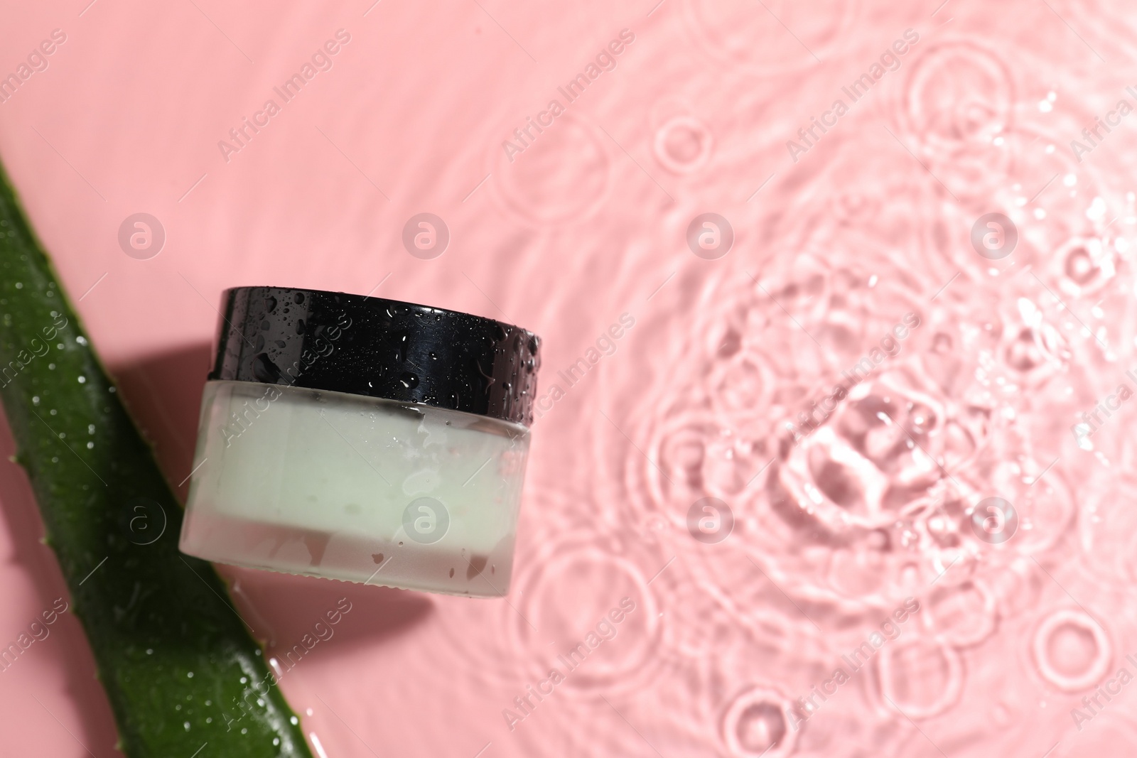 Photo of Jar of cosmetic product and aloe leaf in water on pink background, flat lay. Space for text