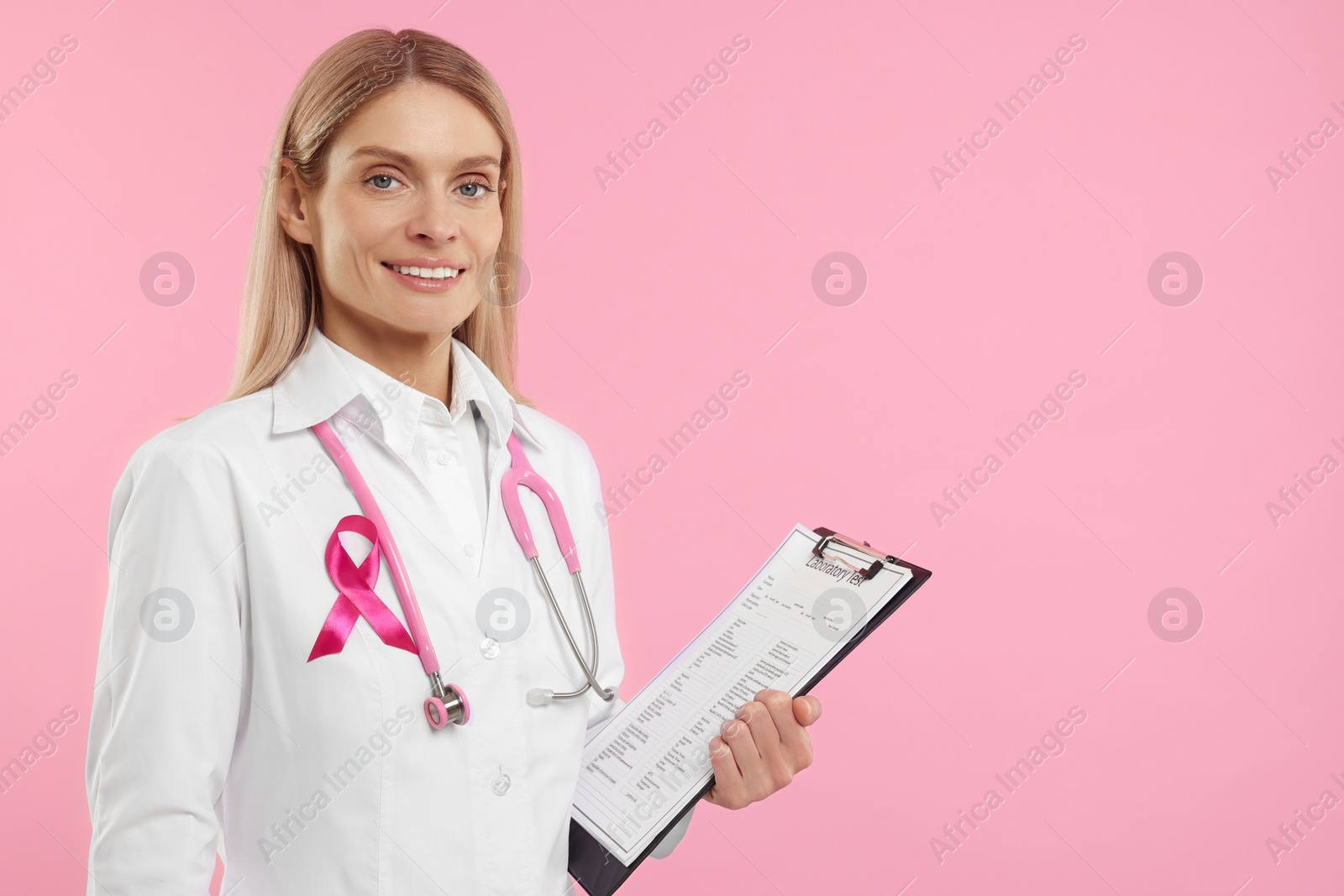 Photo of Doctor with pink ribbon, clipboard and stethoscope on color background, space for text. Breast cancer awareness