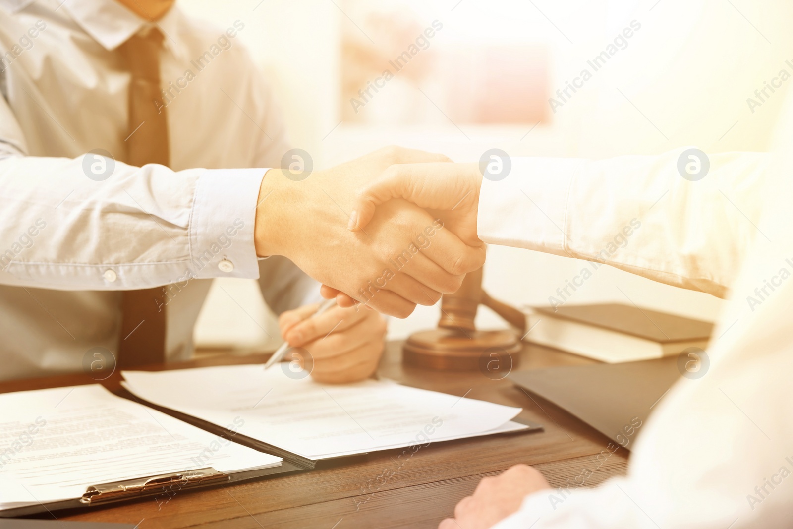 Image of Lawyer shaking hands with client at wooden table in office, closeup