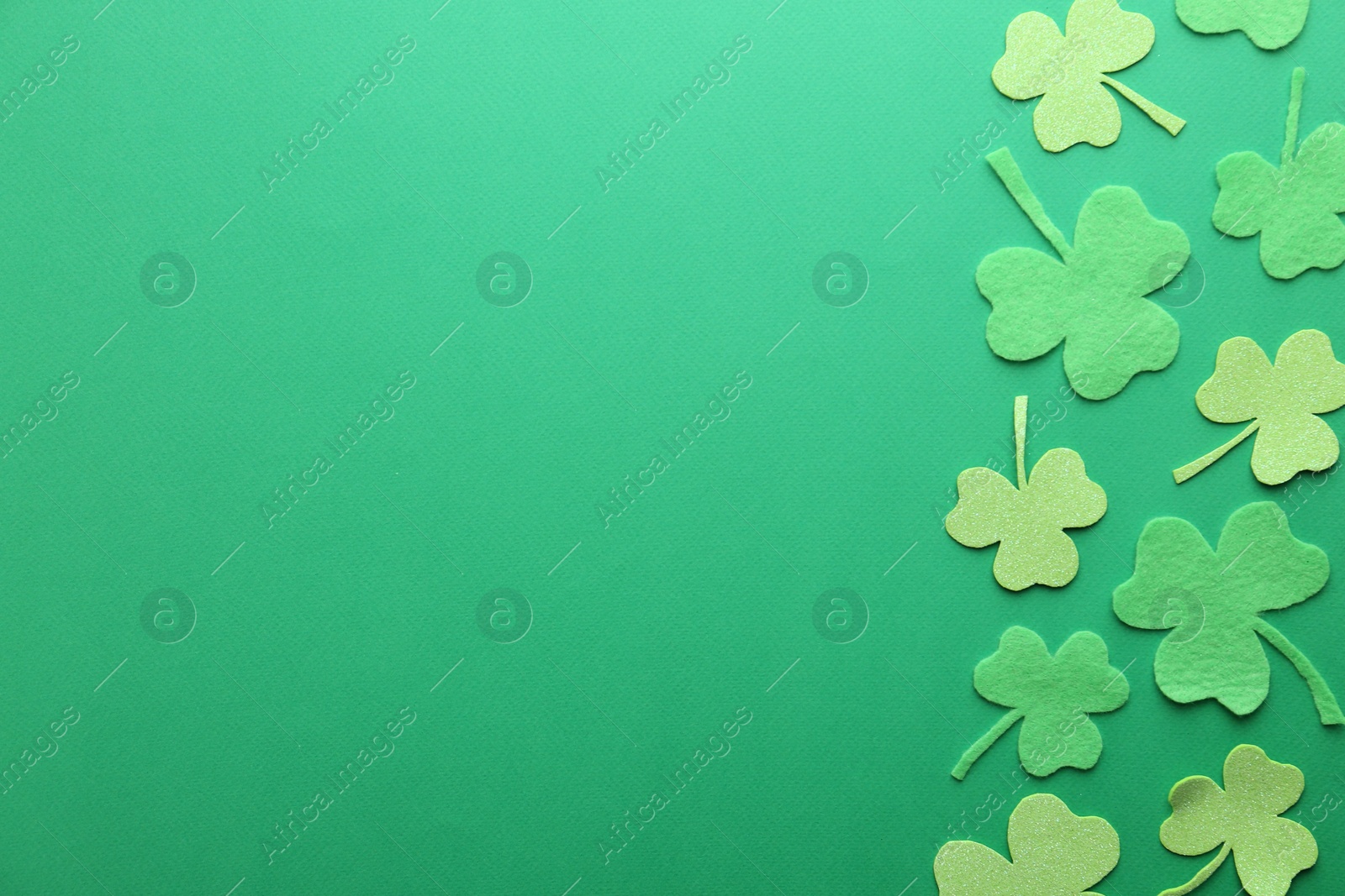 Photo of St. Patrick's day. Decorative clover leaves on green background, flat lay. Space for text