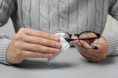 Photo of Man wiping glasses with microfiber cloth at light grey table, closeup