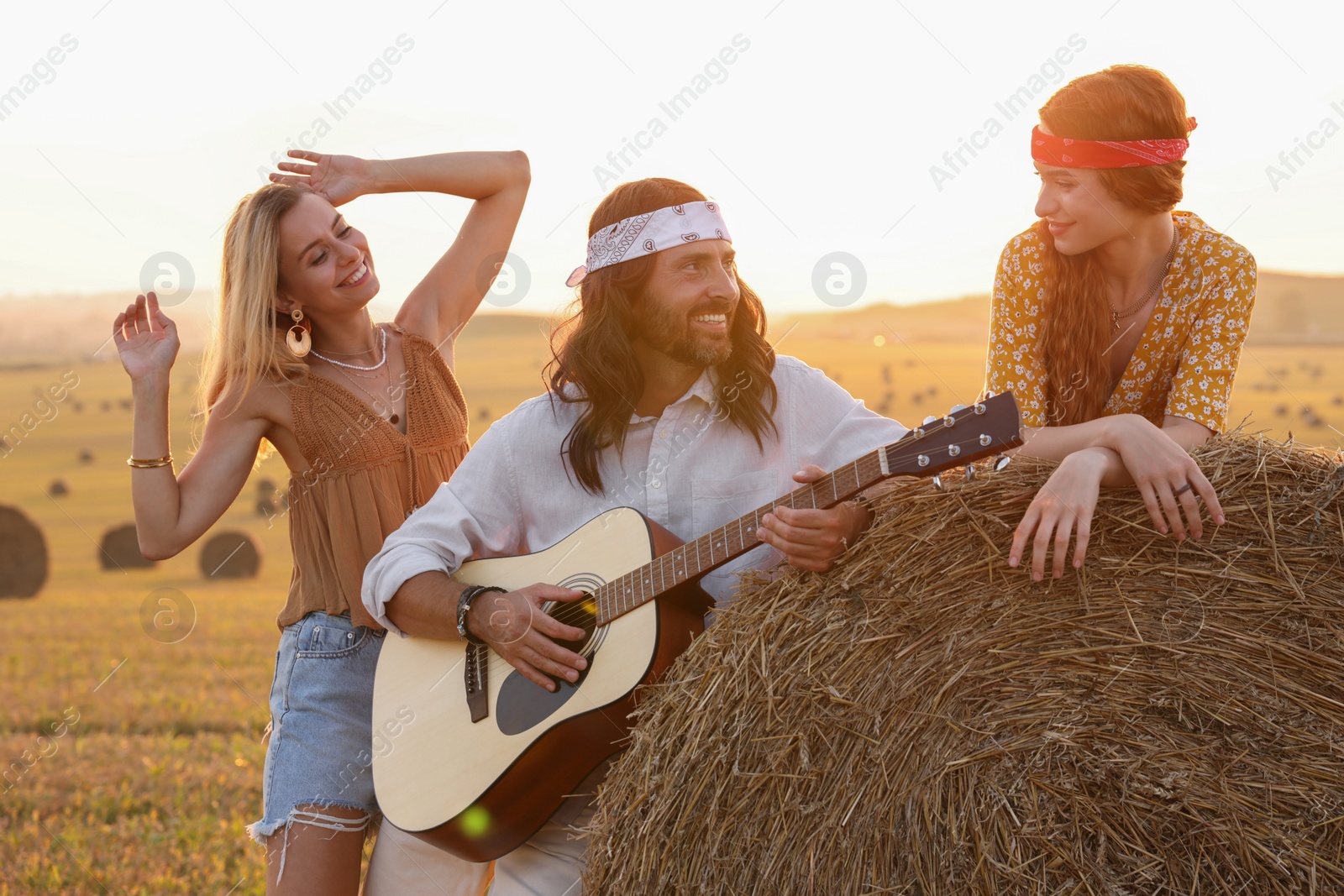 Photo of Beautiful hippie women listening to their friend playing guitar in field