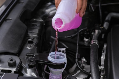 Man pouring liquid from plastic canister into car washer fluid reservoir, closeup