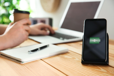 Photo of Man working at table while his mobile phone charging with wireless device