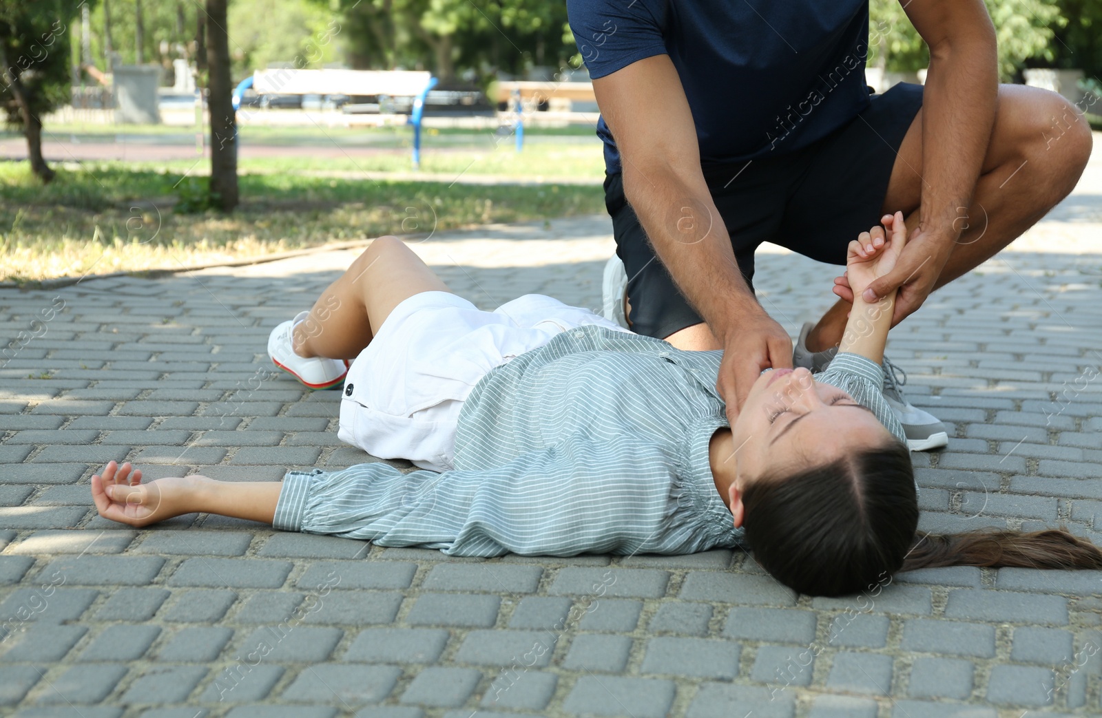 Photo of Man checking pulse of unconscious young woman outdoors. First aid