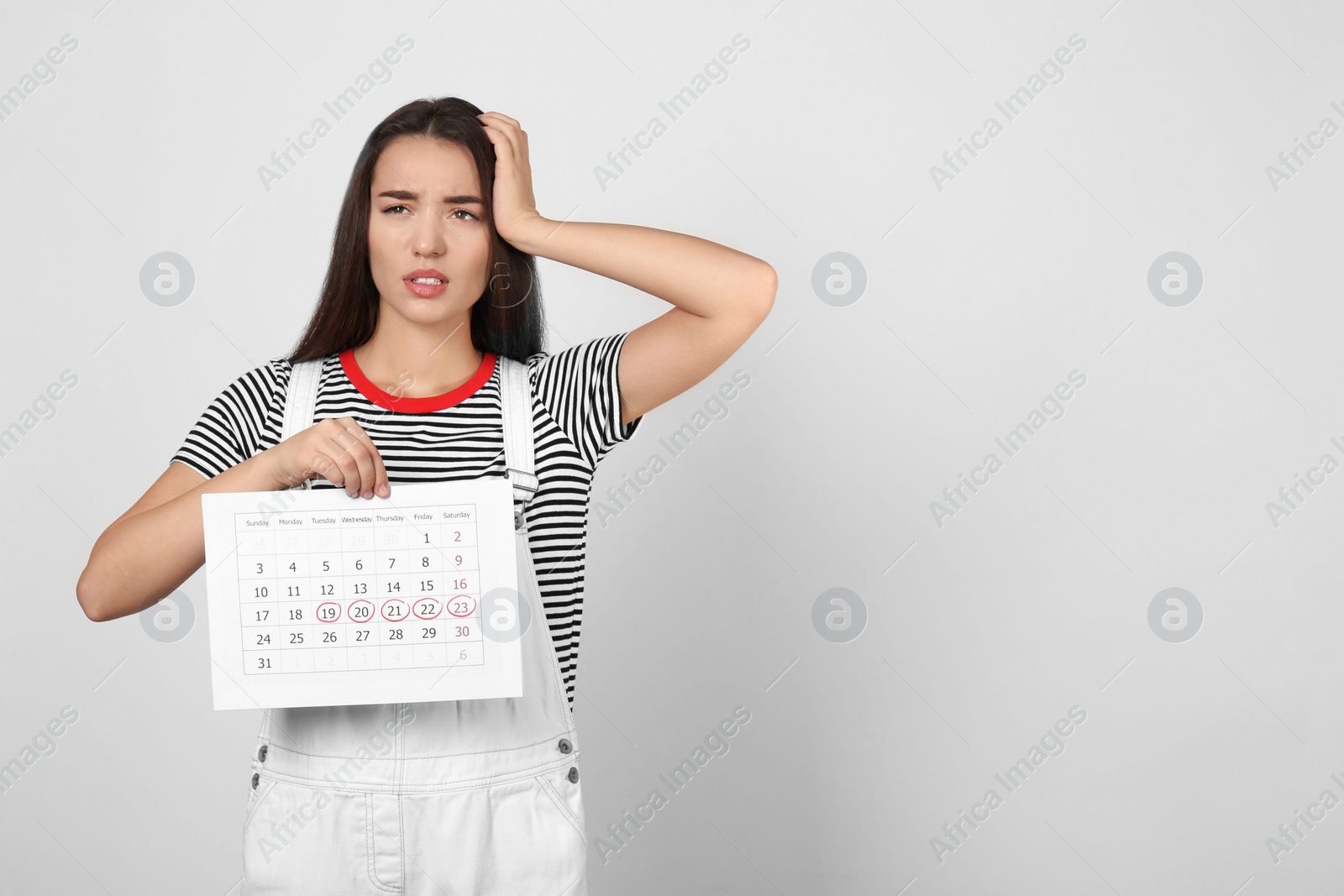 Photo of Young woman holding calendar with marked menstrual cycle days on light background. Space for text