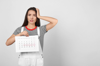 Photo of Young woman holding calendar with marked menstrual cycle days on light background. Space for text