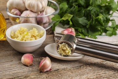 Photo of Garlic press, cloves and mince on wooden table, closeup