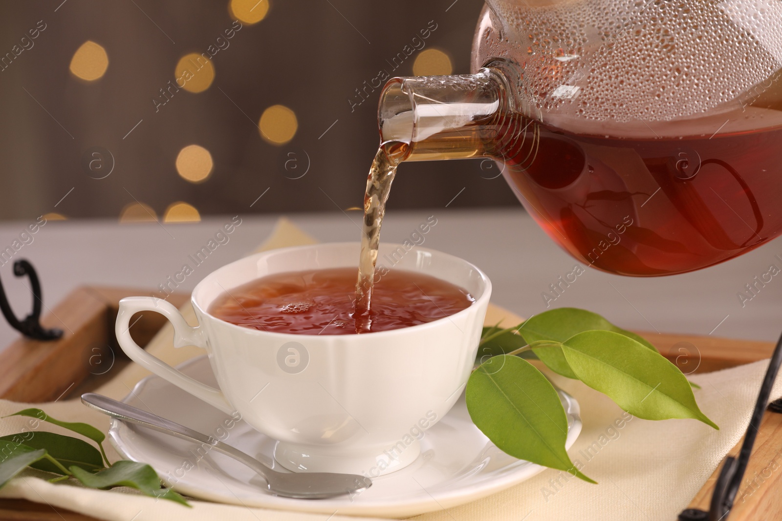 Photo of Pouring aromatic tea into cup at table, closeup