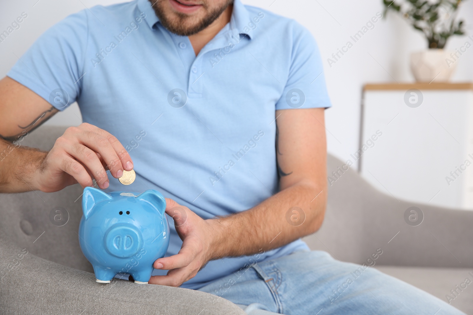 Photo of Young man putting coin into piggy bank in living room