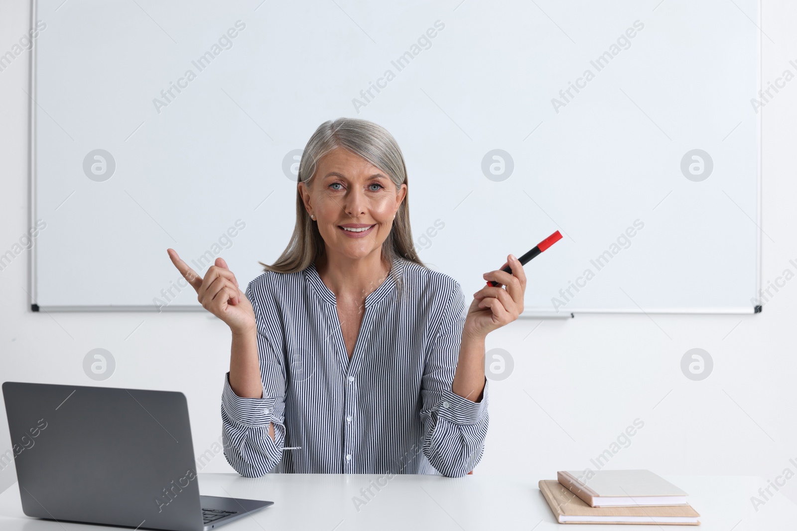 Photo of Happy professor giving lecture near laptop at desk in classroom