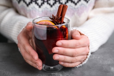 Photo of Woman with glass of mulled wine at grey table, closeup