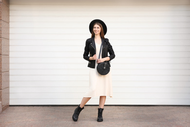 Beautiful young woman with stylish handbag near white wall outdoors