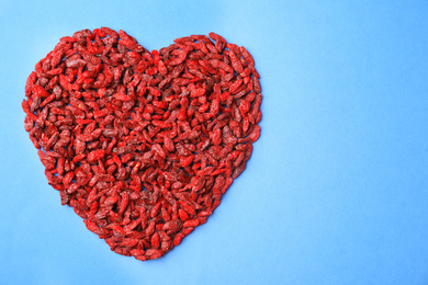 Photo of Heart shaped pile of dried goji berries on blue background, top view. Space for text