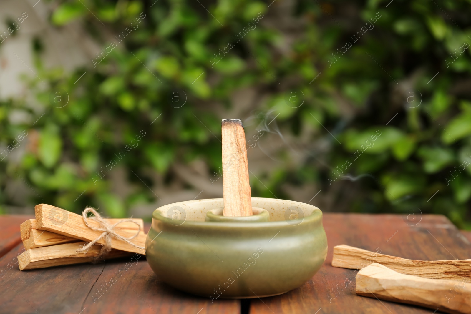 Photo of Palo Santo stick smoldering in holder on wooden table outdoors