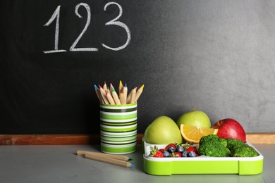 Healthy food for school child in lunch box and stationery on table near blackboard with chalk written numbers