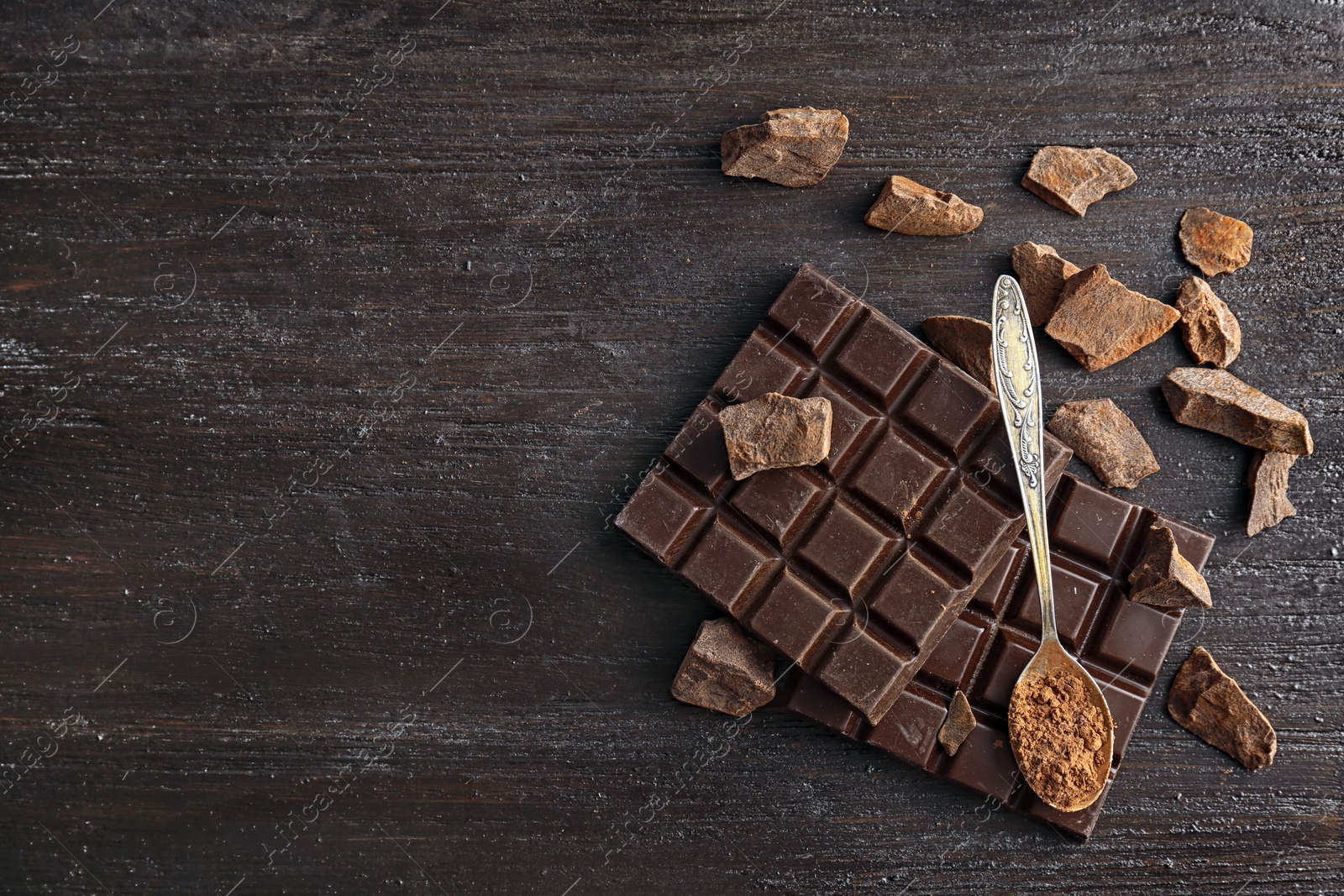 Photo of Spoon with cocoa powder and tasty chocolate on dark table, top view