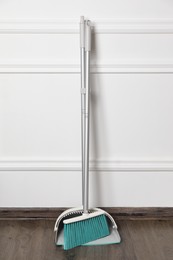 Photo of Plastic broom with dustpan near light wall indoors