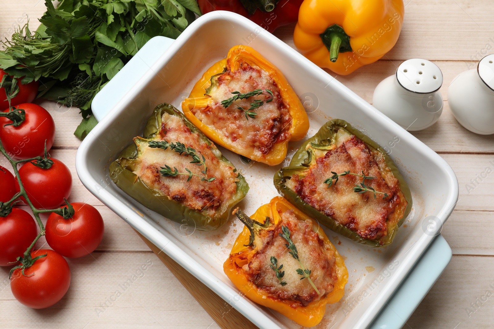 Photo of Tasty stuffed peppers in dish and ingredients on wooden table, flat lay