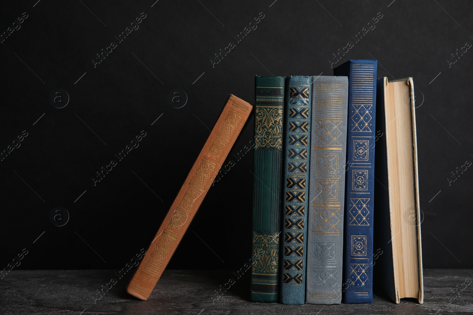 Photo of Stack of hardcover books on grey stone table against dark background