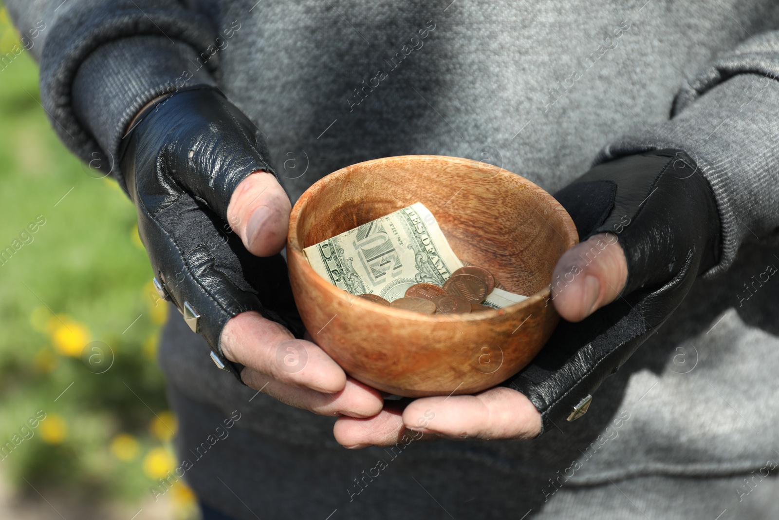 Photo of Poor homeless man holding bowl with donations outdoors, closeup