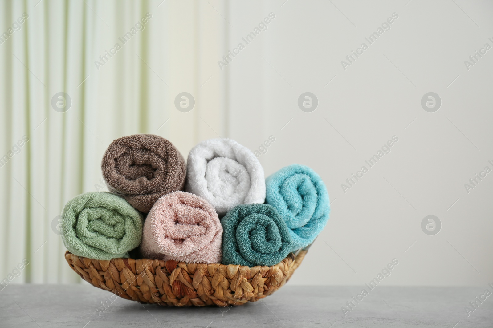 Photo of Rolled color towels on light grey stone table in bathroom. Space for text