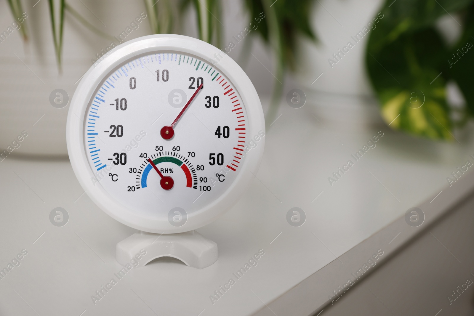 Photo of Round hygrometer with thermometer and plants on white table, space for text