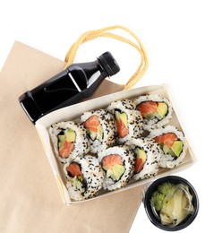Photo of Paper boxes with delicious sushi rolls, bottle of soy sauce and ginger on white background, top view. Food delivery
