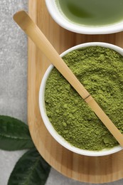 Green matcha powder and bamboo scoop on light grey table, flat lay