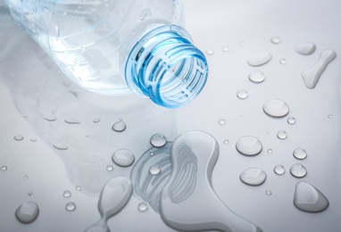 Photo of Drops of spilled water and plastic bottle on grey background, closeup