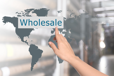 Image of Woman clicking Wholesale button and world map with blurred view of warehouse on background 
