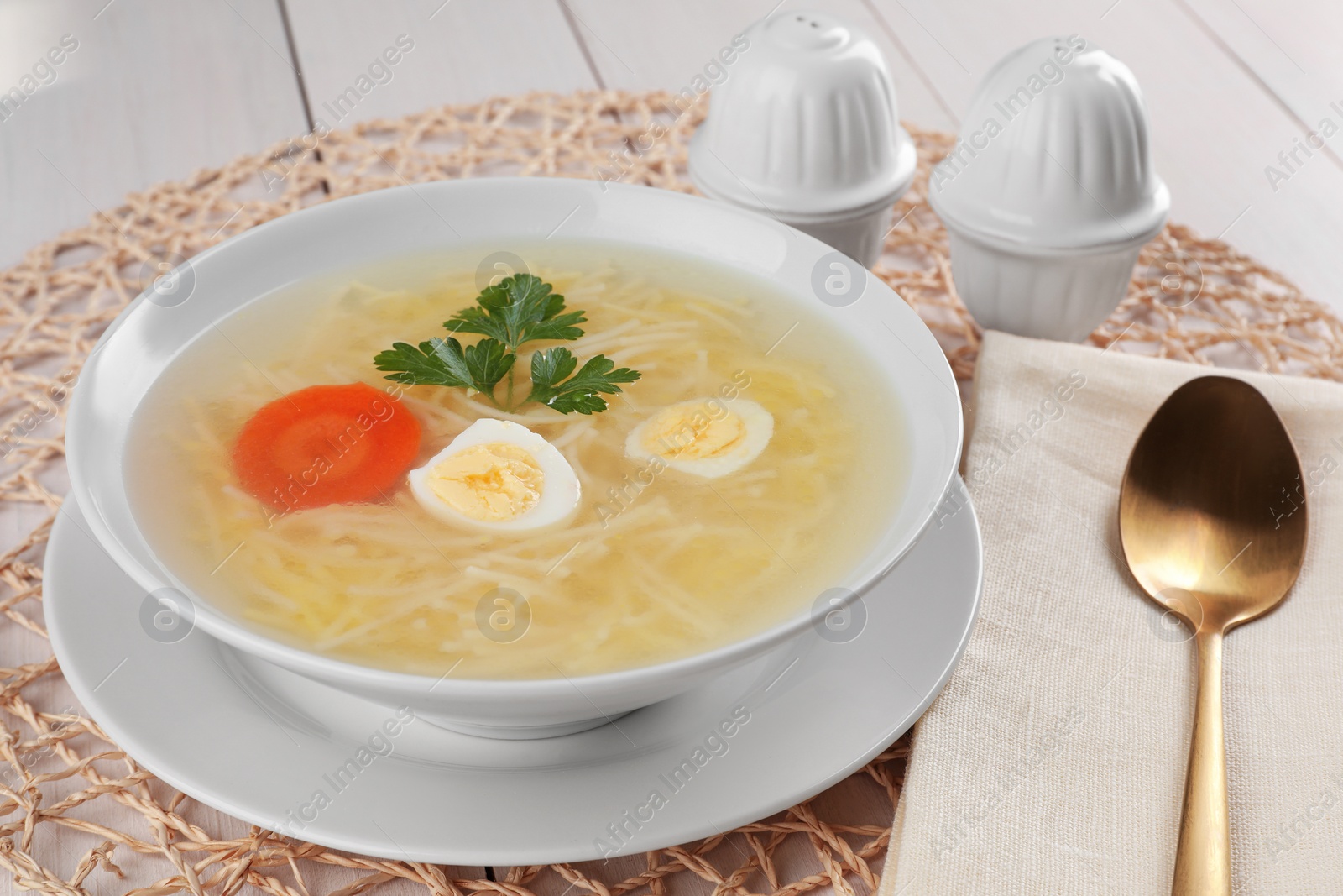 Photo of Tasty soup with noodles, egg, carrot and parsley in bowl served on white wooden table, closeup