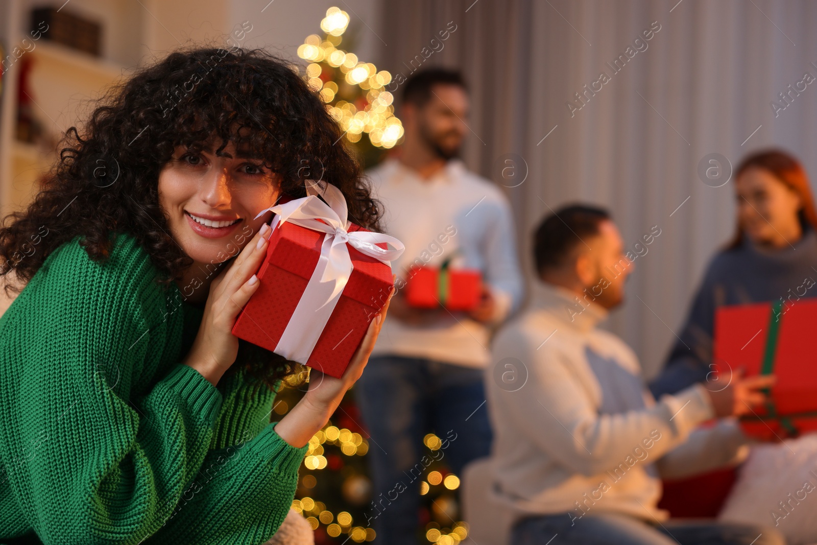 Photo of Christmas celebration in circle of friends. Happy young woman with gift box at home, selective focus