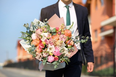 Photo of Man in stylish suit with beautiful flower bouquet on street, closeup view