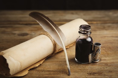 Photo of Feather pen, bottle of ink and parchment scroll on wooden table
