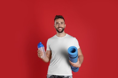 Photo of Handsome man with yoga mat and shaker on red background