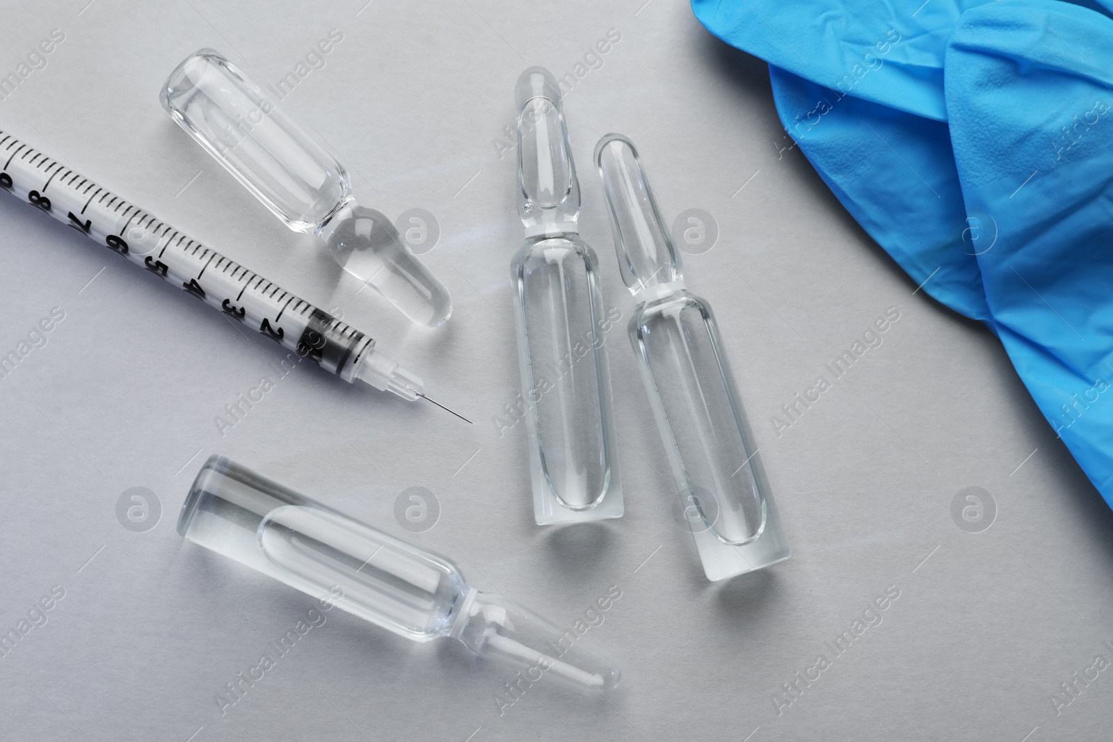 Photo of Pharmaceutical ampoules, gloves and syringe on light background, flat lay