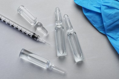 Pharmaceutical ampoules, gloves and syringe on light background, flat lay