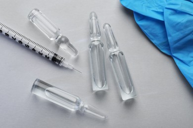 Photo of Pharmaceutical ampoules, gloves and syringe on light background, flat lay