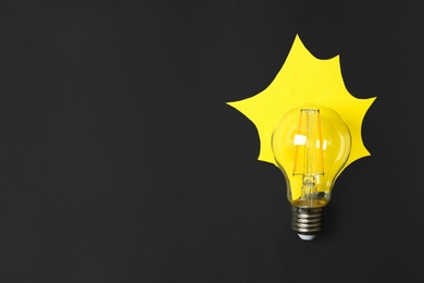 Photo of Lamp bulb with yellow paper imitating light on black background, flat lay