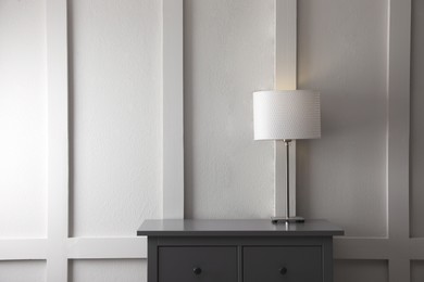 Photo of Wooden chest of drawers with lamp near white wall in room, space for text