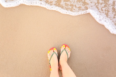 Photo of Top view of woman with stylish flip flops on sand near sea, space for text. Beach accessories