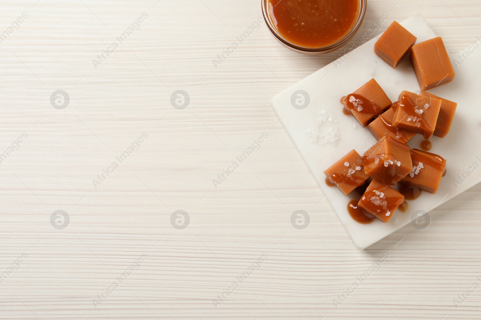 Photo of Tasty caramel candies with sauce and sea salt on white wooden table, flat lay. Space for text