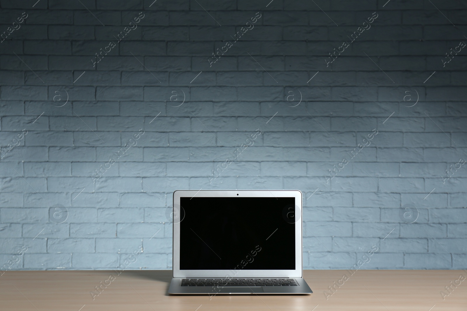 Photo of Modern laptop with blank screen on table against brick wall