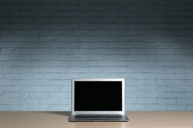 Modern laptop with blank screen on table against brick wall