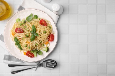 Delicious pasta primavera with tomatoes, basil and broccoli served on white tiled table, flat lay. Space for text