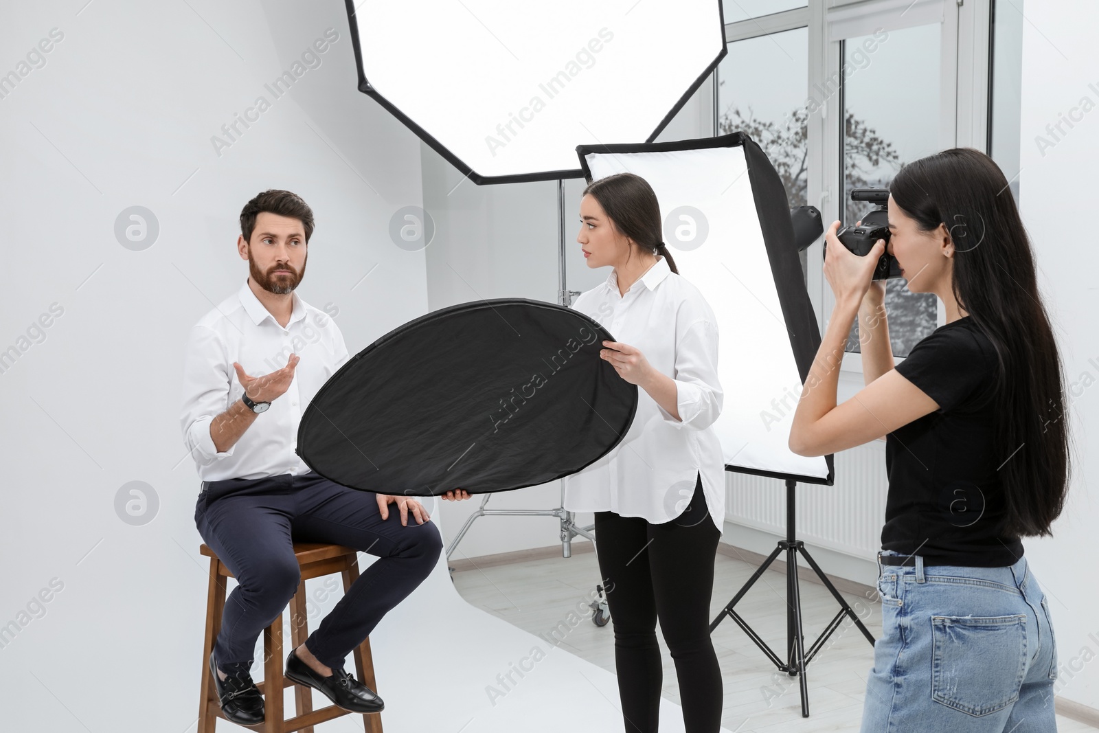 Photo of Professional photographer and assistant working with handsome model in modern photo studio