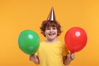 Photo of Happy little boy in party hat with balloons on orange background